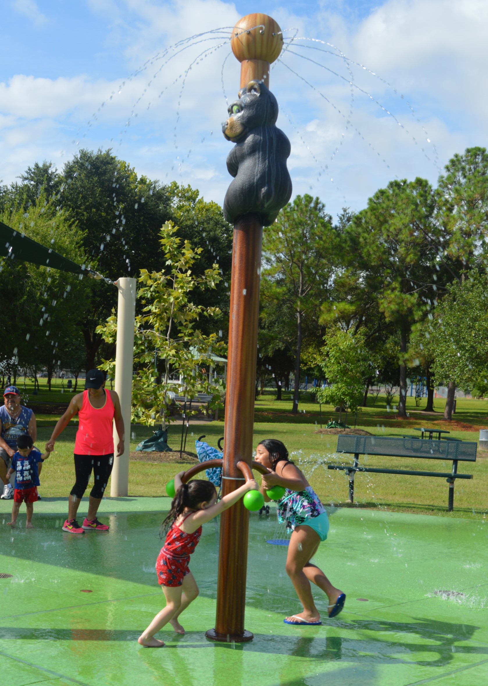 Kids playing outside at Splash Pad with adult in the background